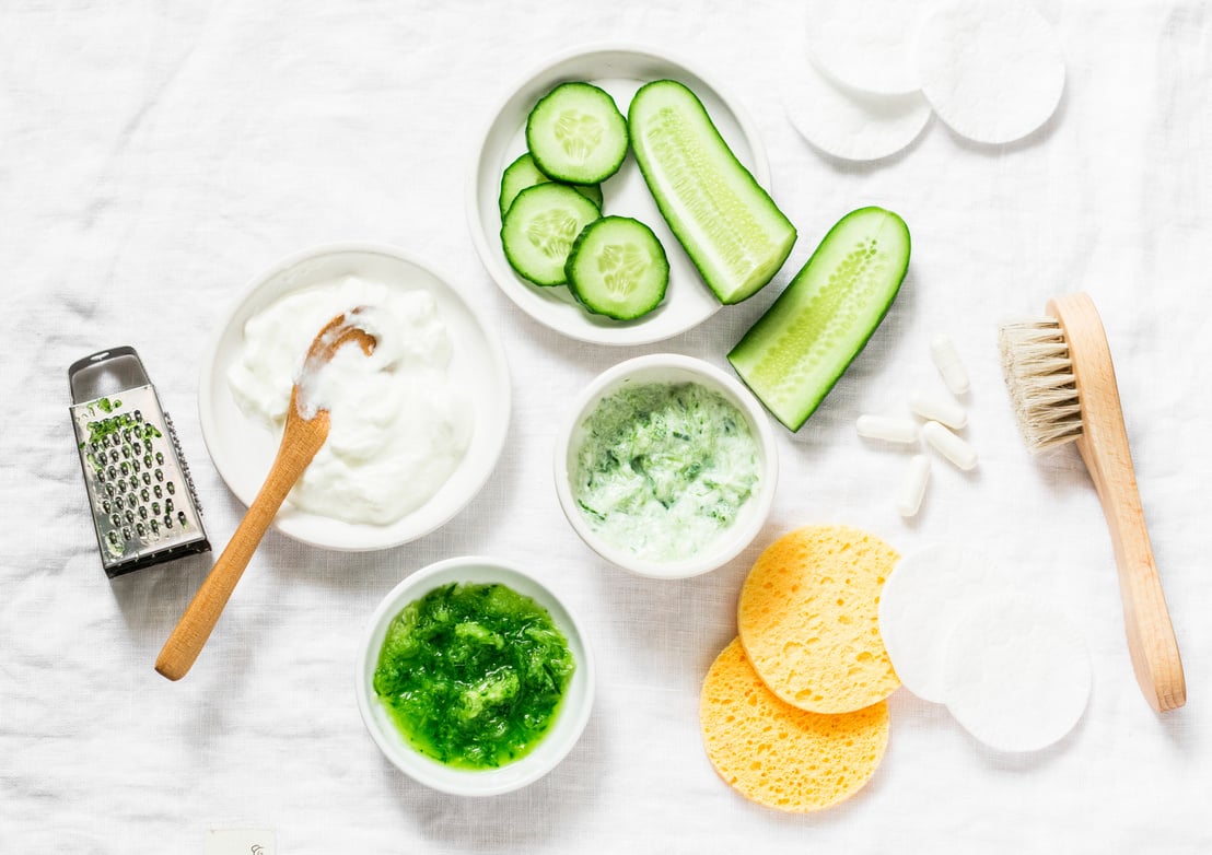 Calming cucumber yogurt mask. Ingredients for homemade cucumber face mask-cucumber, natural yogurt, probiotic capsule, sponges, brush on white background, top view. Flat lay